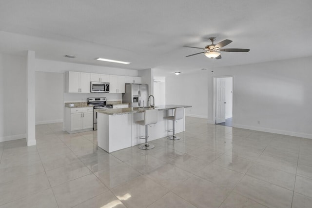 6650 NW 22nd Ct, Margate, FL 33063 - kitchen with stainless steel appliances, a ceiling fan, a kitchen island with sink, white cabinetry, and a kitchen bar