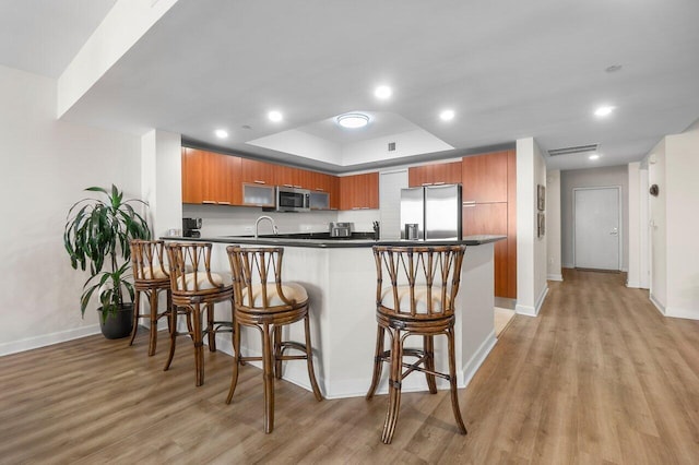 2640 Lake Shore Dr Unit 2409, Riviera Beach, FL 33404 - kitchen featuring appliances with stainless steel finishes, brown cabinetry, a peninsula, a tray ceiling, and baseboards