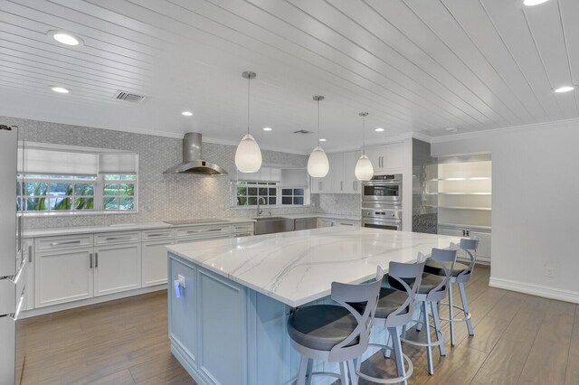 4040 Gem Lake Dr, Glen Ridge, FL 33406 - kitchen featuring wall chimney exhaust hood, black electric cooktop, white cabinetry, a center island, and light stone counters