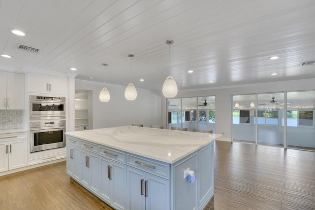 4040 Gem Lake Dr, Glen Ridge, FL 33406 - kitchen with stainless steel double oven, a center island, wood finished floors, light stone counters, and ornamental molding