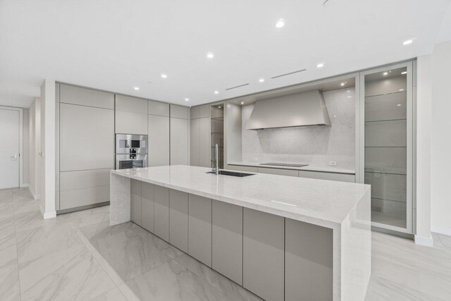 220 SE Mizner Blvd Unit 409, Boca Raton, FL 33432 - kitchen with gray cabinets, modern cabinets, wall chimney range hood, a sink, and a large island with sink