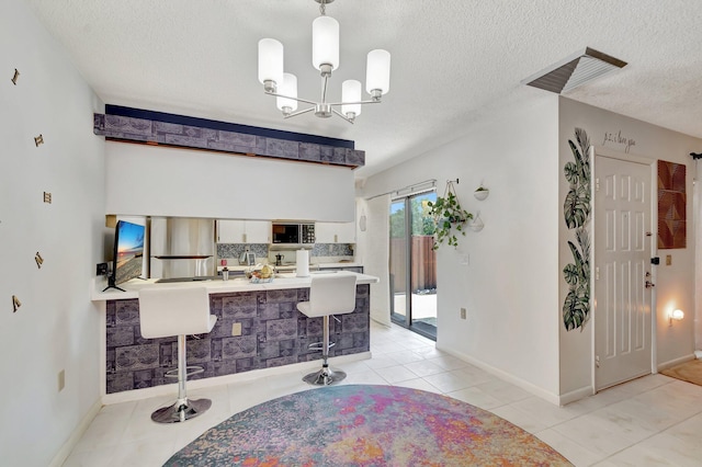 6644 66th Way, West Palm Beach, FL 33409 - kitchen with backsplash, a textured ceiling, a peninsula, a breakfast bar area, and white cabinetry