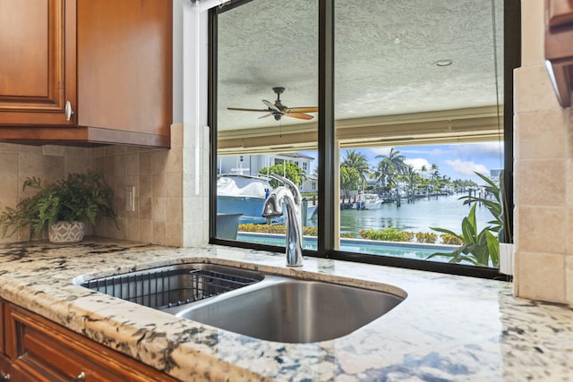 3819 N Ocean Dr, Singer Island, FL 33404 - kitchen featuring a sink, tasteful backsplash, light stone counters, a water view, and ceiling fan