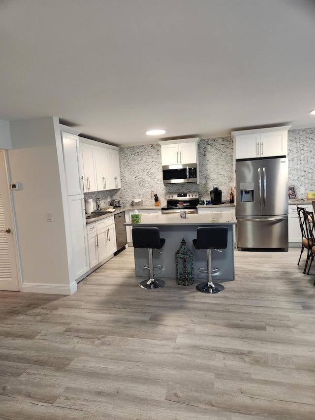 302 Wellington Unit B, West Palm Beach, FL 33417 - kitchen with appliances with stainless steel finishes, backsplash, a center island, white cabinets, and light wood finished floors