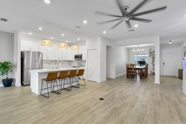3974 SW Jarmer Rd, Port Saint Lucie, FL 34953 - kitchen featuring stainless steel appliances, a kitchen island with sink, light wood finished floors, a kitchen breakfast bar, and backsplash