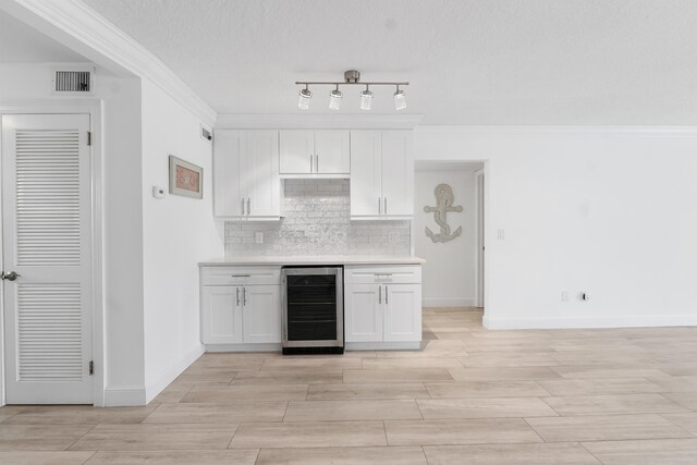 109 Wettaw Ln Unit 103, North Palm Beach, FL 33408 - kitchen featuring beverage cooler, white cabinets, backsplash, light countertops, and ornamental molding