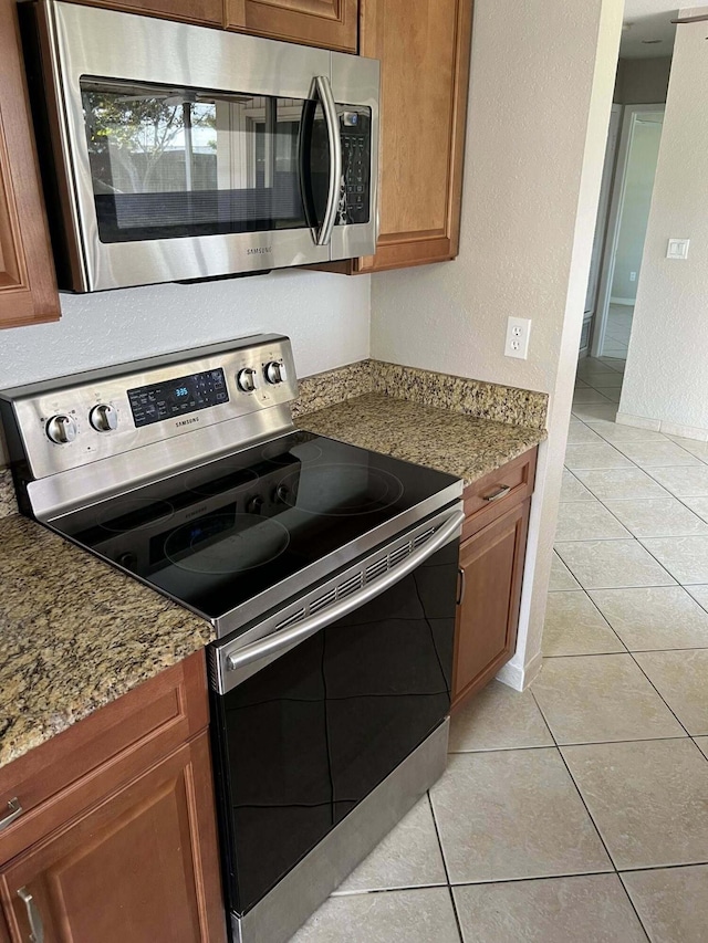 318 NW Byron St, Port Saint Lucie, FL 34983 - kitchen featuring appliances with stainless steel finishes, light tile patterned floors, brown cabinetry, and light stone counters