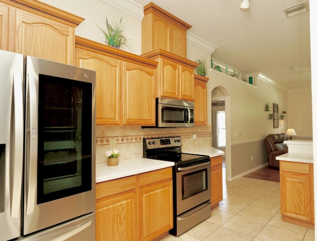 1985 SW Glenco St, Port Saint Lucie, FL 34953 - kitchen featuring stainless steel appliances, crown molding, decorative backsplash, light tile patterned floors, and arched walkways