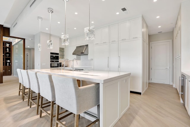 1 N Ocean Blvd Unit Ph05, Pompano Beach, FL 33062 - kitchen with light wood-style floors, under cabinet range hood, a sink, white cabinets, and a large island with sink