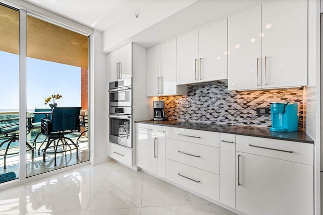 2640 Lake Shore Dr Unit 2307, Riviera Beach, FL 33404 - kitchen with dark countertops, decorative backsplash, light marble finish floors, white cabinets, and floor to ceiling windows