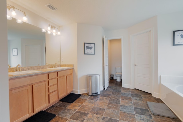 517 SW Cherryhill Rd, Port Saint Lucie, FL 34953 - bathroom featuring baseboards, double vanity, stone finish floors, a bath, and toilet