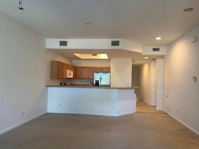 10280 SW Stephanie Way Unit 8209, Port Saint Lucie, FL 34987 - kitchen featuring stainless steel fridge with ice dispenser, white microwave, baseboards, brown cabinetry, and a peninsula