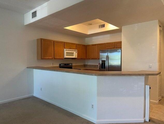 10280 SW Stephanie Way Unit 8209, Port Saint Lucie, FL 34987 - kitchen featuring stainless steel fridge, white microwave, brown cabinets, a peninsula, and stove