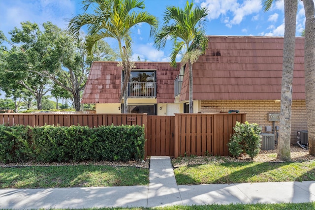 744 Buttonwood Ln Unit 411-D, Boynton Beach, FL 33436 - view of home's exterior featuring brick siding, a fenced front yard, mansard roof, and central AC
