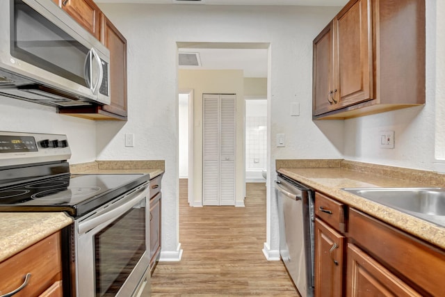 5171 Glencove Ln, West Palm Beach, FL 33415 - kitchen with stainless steel appliances, light wood finished floors, baseboards, light countertops, and brown cabinetry
