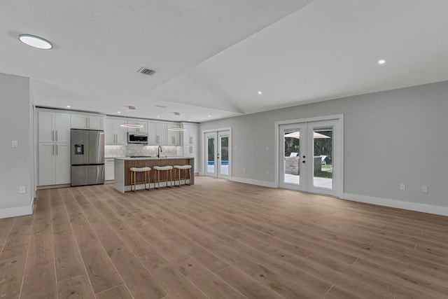 18228 48th Ave N, The Acreage, FL 33470 - unfurnished living room featuring french doors, a sink, baseboards, light wood-type flooring, and vaulted ceiling