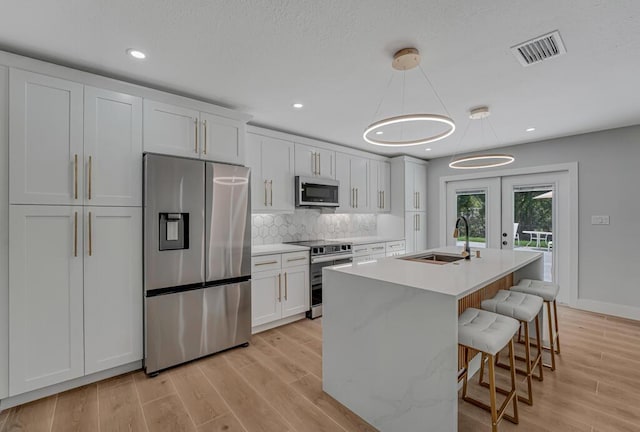 18228 48th Ave N, The Acreage, FL 33470 - kitchen featuring stainless steel appliances, a sink, a center island with sink, white cabinetry, and tasteful backsplash