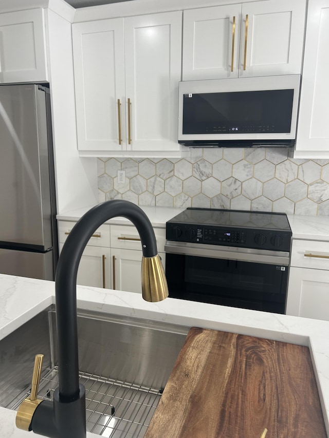 18228 48th Ave N, The Acreage, FL 33470 - kitchen view of black electric range, freestanding refrigerator, white cabinets, tasteful backsplash, and light stone countertops