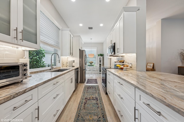 5096 SE Sweetbrier Ter, Hobe Sound, FL 33455 - kitchen featuring appliances with stainless steel finishes, a sink, light wood finished floors, white cabinetry, and light stone countertops