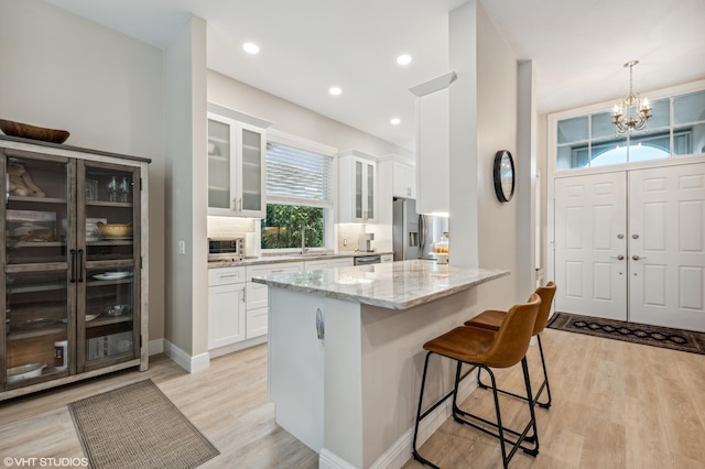 5096 SE Sweetbrier Ter, Hobe Sound, FL 33455 - kitchen featuring stainless steel refrigerator with ice dispenser, a kitchen breakfast bar, light stone countertops, white cabinetry, and a chandelier