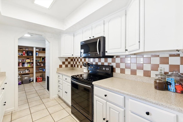 1430 SE Ocean Ln, Port Saint Lucie, FL 34983 - kitchen featuring black electric range oven, stainless steel microwave, light tile patterned floors, white cabinets, and decorative backsplash