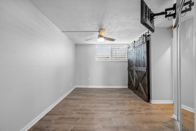 104 Paradise Harbour Blvd Unit 104, North Palm Beach, FL 33408 - unfurnished bedroom with a textured ceiling, wood finished floors, a barn door, baseboards, and ceiling fan