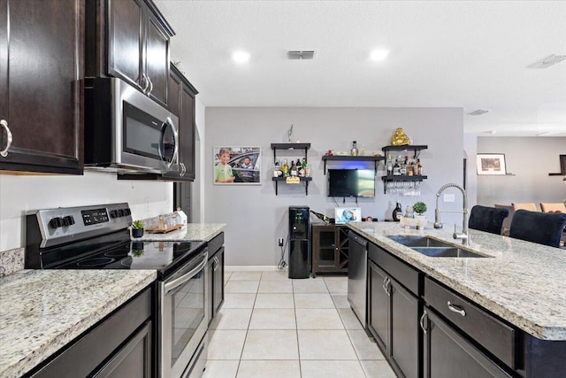 3313 SW Ludlow St, Port Saint Lucie, FL 34953 - kitchen featuring appliances with stainless steel finishes, a sink, light stone counters, light tile patterned floors, and a center island with sink