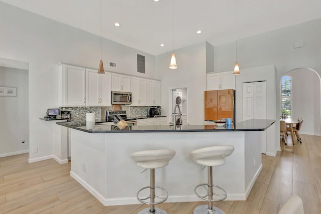 2703 SW Glenmoor Way, Palm City, FL 34990 - kitchen featuring appliances with stainless steel finishes, dark countertops, arched walkways, a high ceiling, and white cabinetry