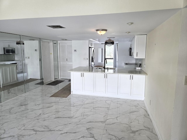 1731 Presidential Way Unit C201, West Palm Beach, FL 33401 - kitchen featuring appliances with stainless steel finishes, light marble finish flooring, white cabinets, a peninsula, and light countertops