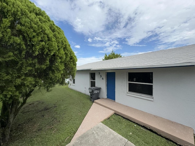 324W W 5th Ter, Pahokee, FL 33476 - property entrance featuring a lawn, stucco siding, covered porch, and a shingled roof