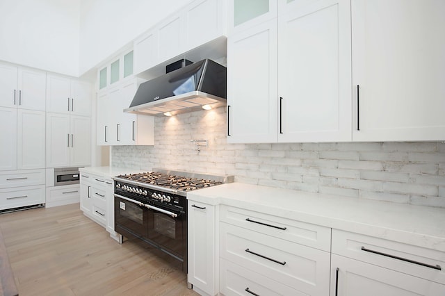 18072 127th Dr N, Jupiter, FL 33478 - kitchen featuring range with two ovens, wall chimney exhaust hood, backsplash, light countertops, and white cabinets