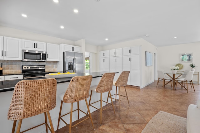 330 SE 7th Ave, Delray Beach, FL 33483 - kitchen featuring appliances with stainless steel finishes, backsplash, dark countertops, a breakfast bar area, and white cabinetry