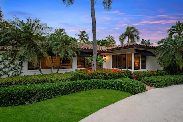 330 SE 7th Ave, Delray Beach, FL 33483 - back of property at dusk featuring a yard, stucco siding, and a tiled roof