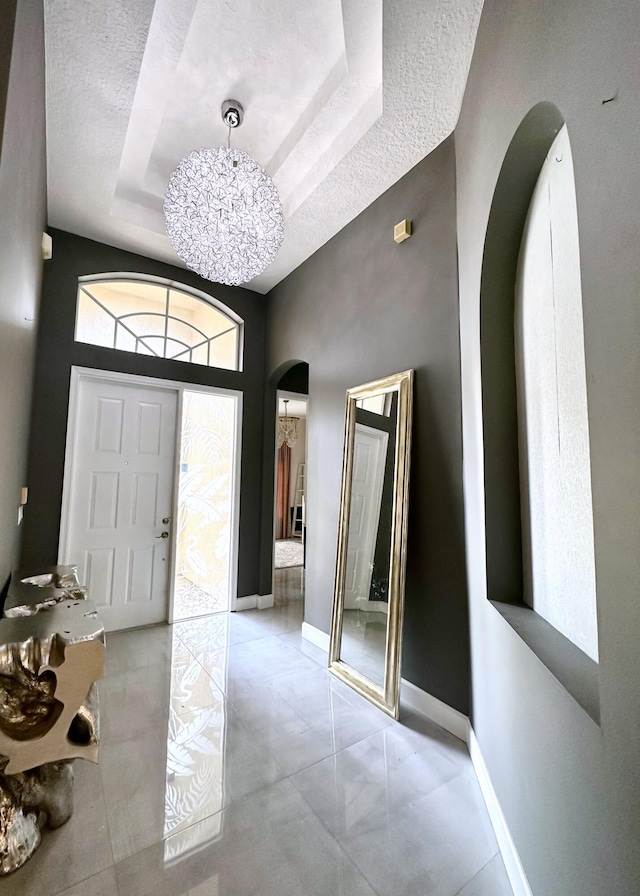 8825 Gibson Cay, West Palm Beach, FL 33411 - entrance foyer with arched walkways, a textured ceiling, a raised ceiling, baseboards, and a chandelier