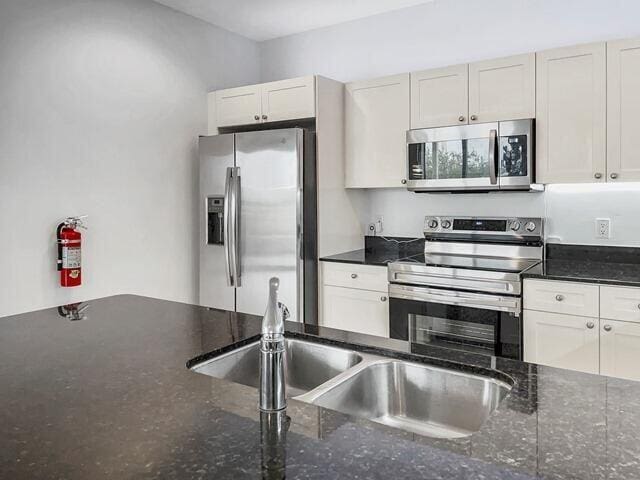 3960 N Flagler Dr Unit 305, West Palm Beach, FL 33407 - kitchen featuring appliances with stainless steel finishes, dark stone countertops, white cabinetry, and a sink