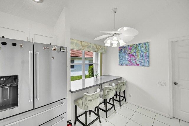 6078 Slice Ct, Boynton Beach, FL 33437 - kitchen featuring stainless steel fridge, ceiling fan, light tile patterned floors, a breakfast bar, and white cabinets