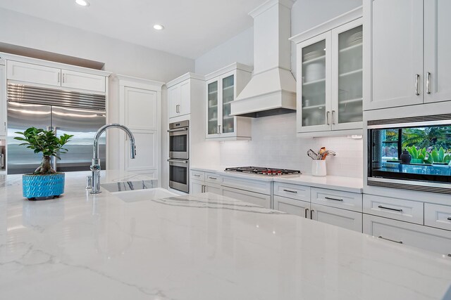 8164 SE Old Plantation Cir, Jupiter, FL 33458 - kitchen with built in appliances, a sink, custom range hood, white cabinets, and backsplash