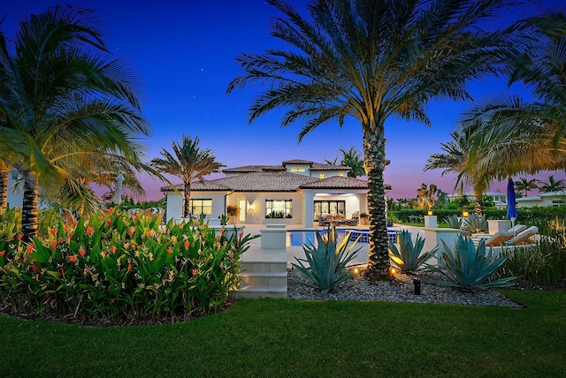 8164 SE Old Plantation Cir, Jupiter, FL 33458 - back of property at dusk featuring a tile roof, stucco siding, a yard, and a swimming pool
