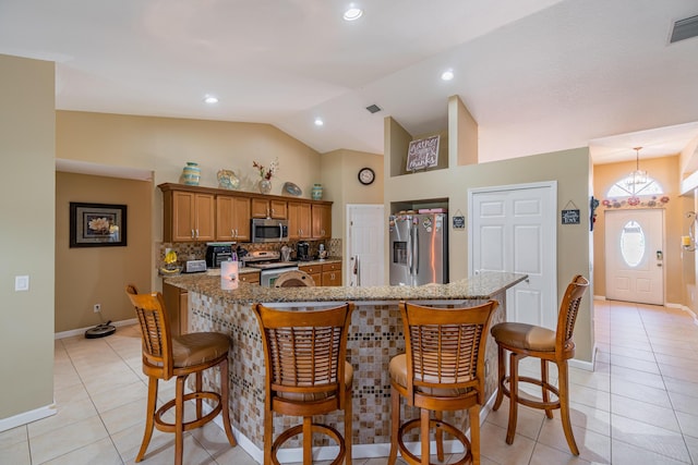 3542 SW Rosardo St, Port Saint Lucie, FL 34953 - kitchen featuring stainless steel appliances, light tile patterned floors, brown cabinetry, lofted ceiling, and a breakfast bar