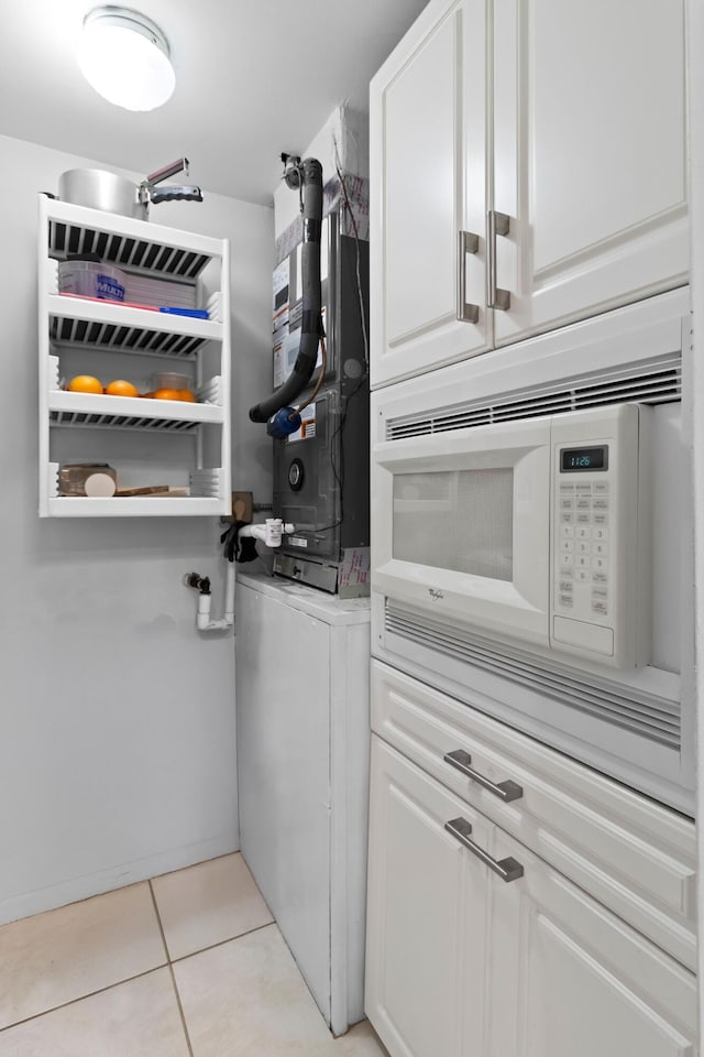 437 Pine Glen Ln Unit B-2, Greenacres, FL 33463 - kitchen featuring stacked washing machine and dryer, white microwave, light tile patterned floors, and white cabinetry