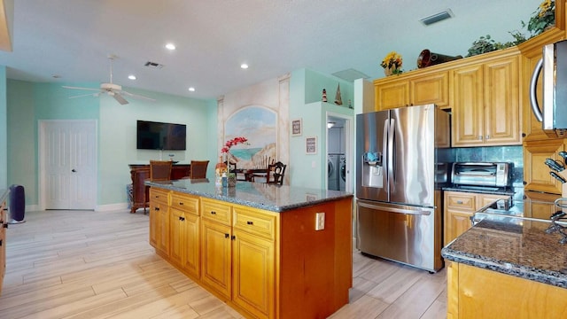 2608 SW River Shore Dr, Port Saint Lucie, FL 34984 - kitchen featuring stainless steel appliances, ceiling fan, light wood-type flooring, dark stone counters, and a center island
