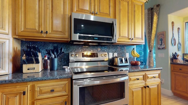 2608 SW River Shore Dr, Port Saint Lucie, FL 34984 - kitchen featuring stainless steel appliances, tasteful backsplash, dark stone countertops, and brown cabinetry