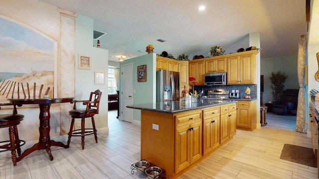 2608 SW River Shore Dr, Port Saint Lucie, FL 34984 - kitchen featuring appliances with stainless steel finishes, backsplash, a kitchen island, dark stone countertops, and light wood finished floors