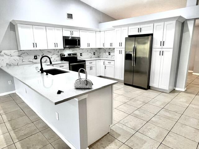 8065 99th Ct, Vero Beach, FL 32967 - kitchen with stainless steel appliances, a peninsula, light tile patterned floors, tasteful backsplash, and lofted ceiling