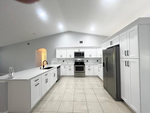 8065 99th Ct, Vero Beach, FL 32967 - kitchen featuring stainless steel appliances, arched walkways, lofted ceiling, a peninsula, and tasteful backsplash