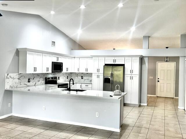 8065 99th Ct, Vero Beach, FL 32967 - kitchen featuring stainless steel appliances, a peninsula, light countertops, lofted ceiling, and tasteful backsplash