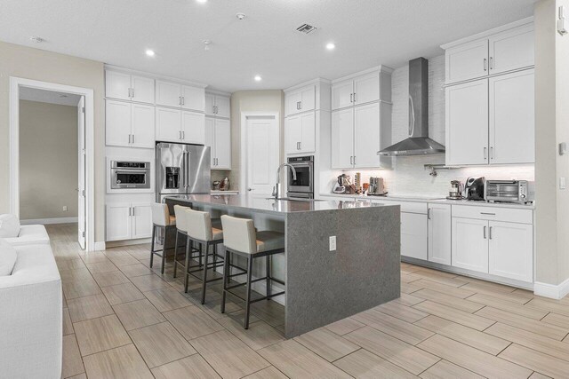 9258 Greenspire Ln, Lake Worth, FL 33467 - kitchen with wall chimney range hood, stainless steel appliances, backsplash, an island with sink, and wood tiled floors