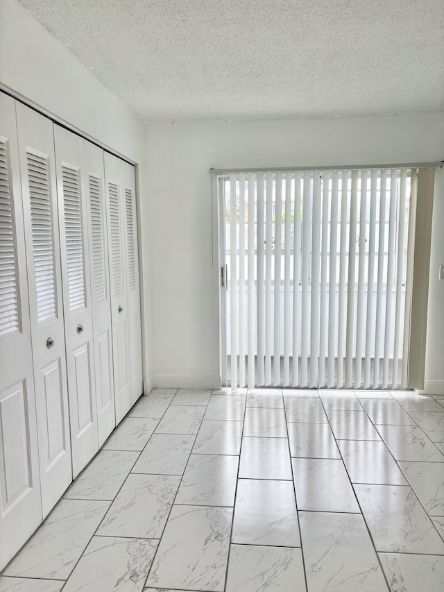 76 Cambridge Unit D, West Palm Beach, FL 33417 - unfurnished bedroom with marble finish flooring, a textured ceiling, a closet, and baseboards
