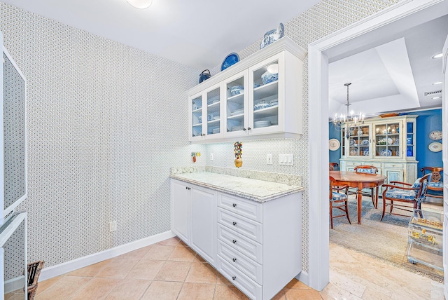 2160 Ibis Isle Rd Unit 9, Palm Beach, FL 33480 - kitchen featuring glass insert cabinets, light stone counters, white cabinetry, a chandelier, and a raised ceiling