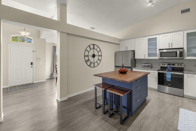 4312 SW Elaine Ct, Port Saint Lucie, FL 34953 - kitchen with appliances with stainless steel finishes, butcher block counters, a kitchen bar, decorative backsplash, and white cabinetry